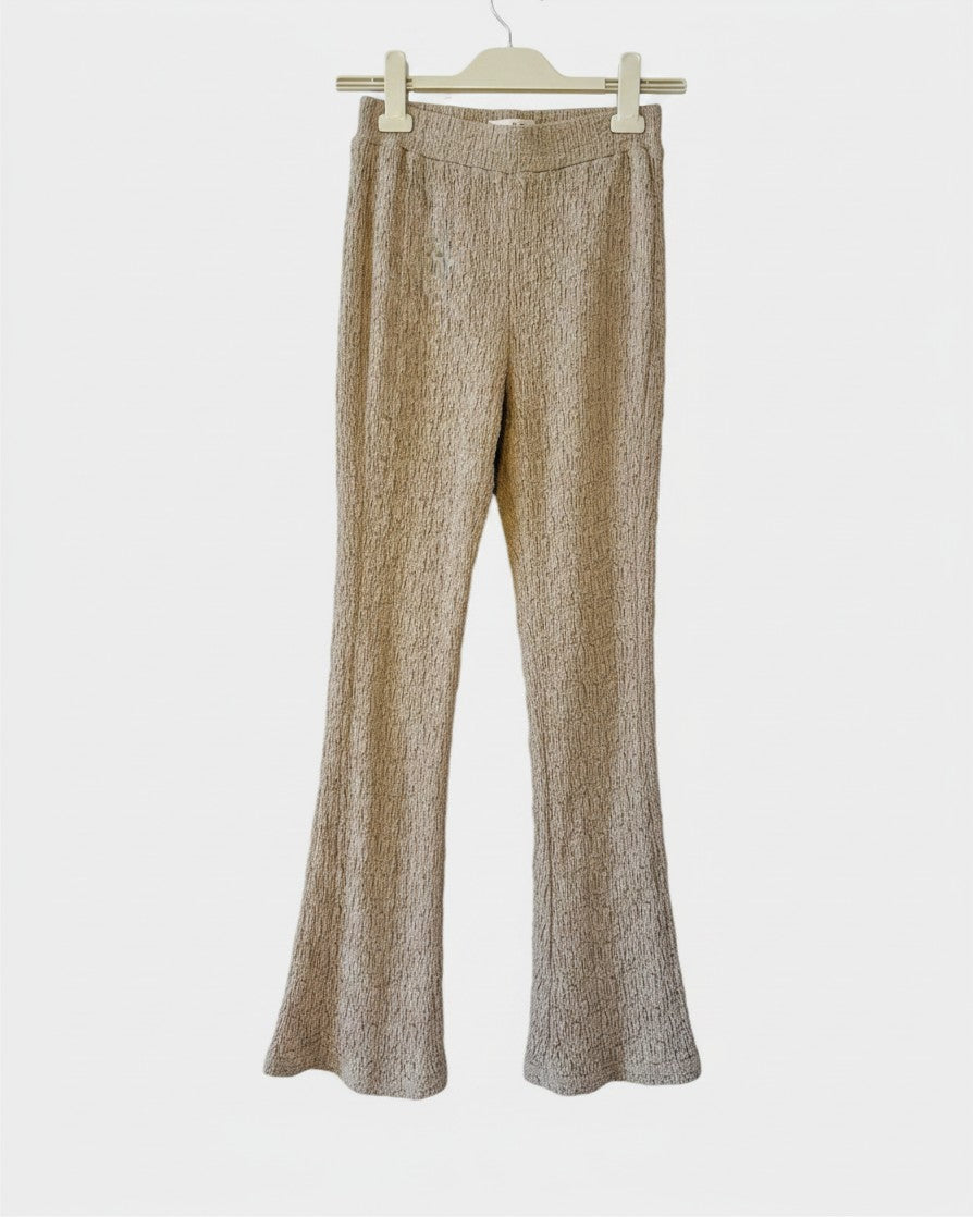 Lula and Mimi ODE knit trousers in a textured beige fabric with a flared leg silhouette hanging on a hanger.